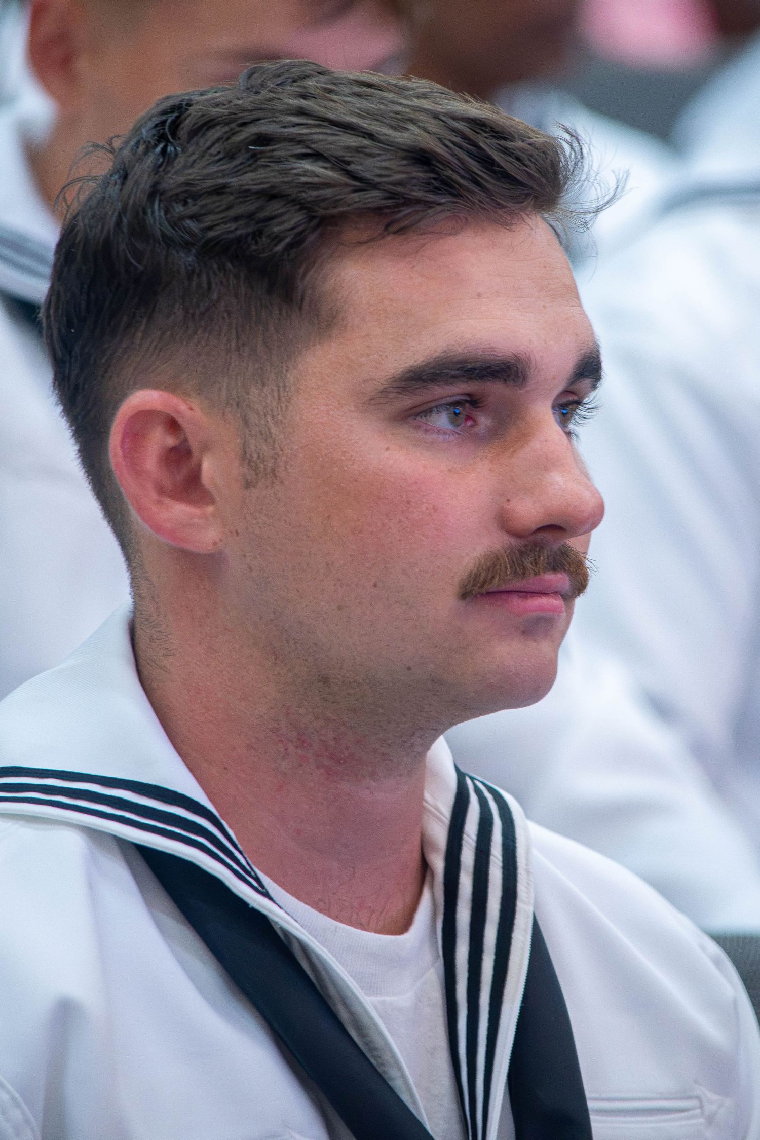 Male US Navy sailor with mustache in profile wearing white dress uniform.