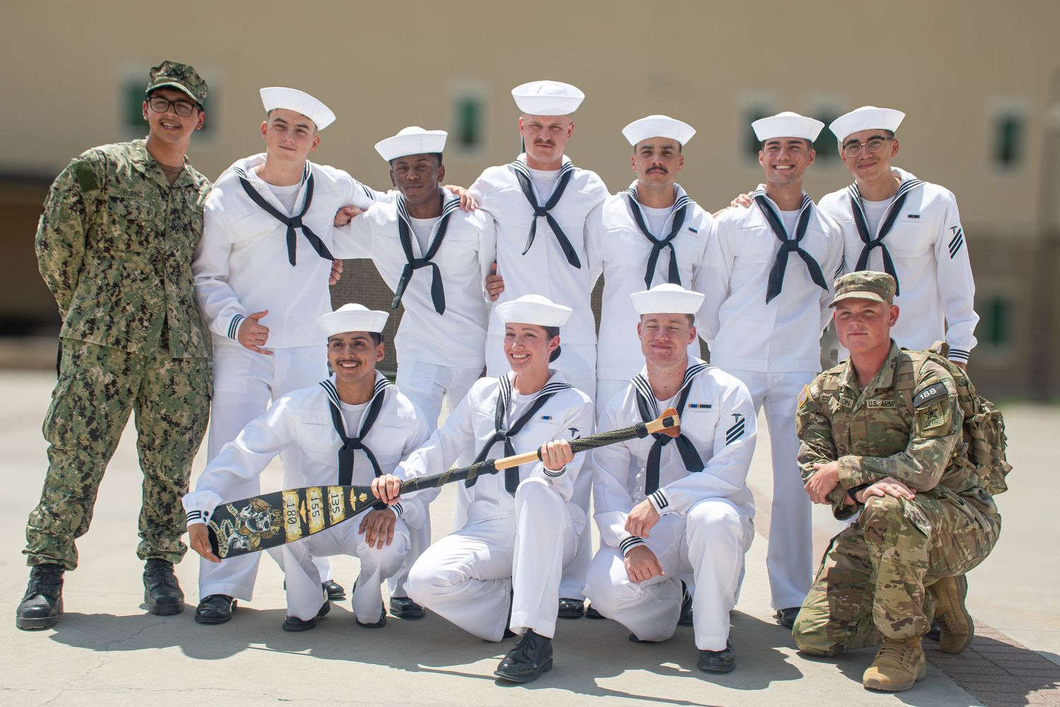 Group of Navy sailors in dress whites pose with trophy flanked by two officers in camouflage.