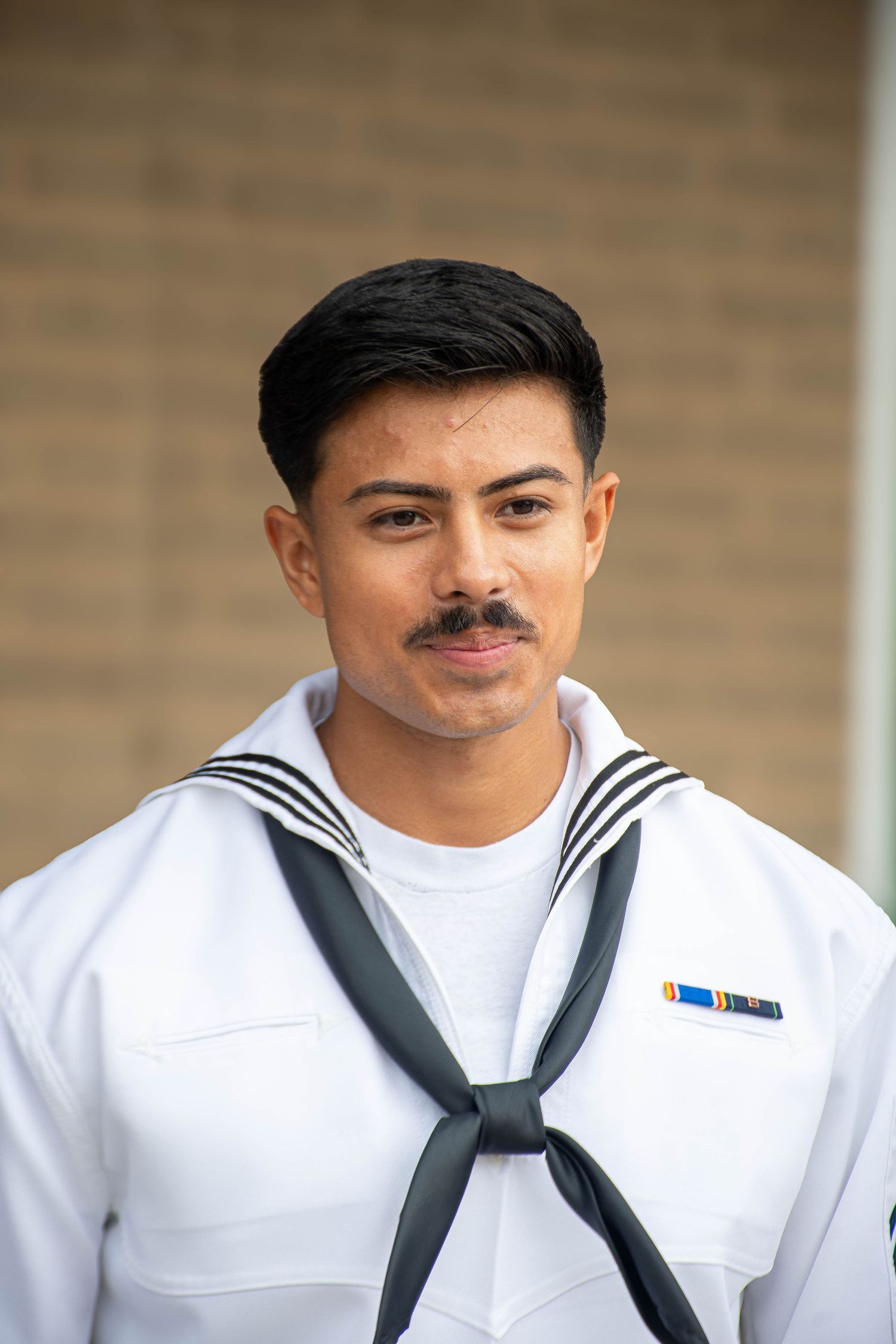 Young Navy sailor in dress whites uniform with service ribbon poses outdoors.