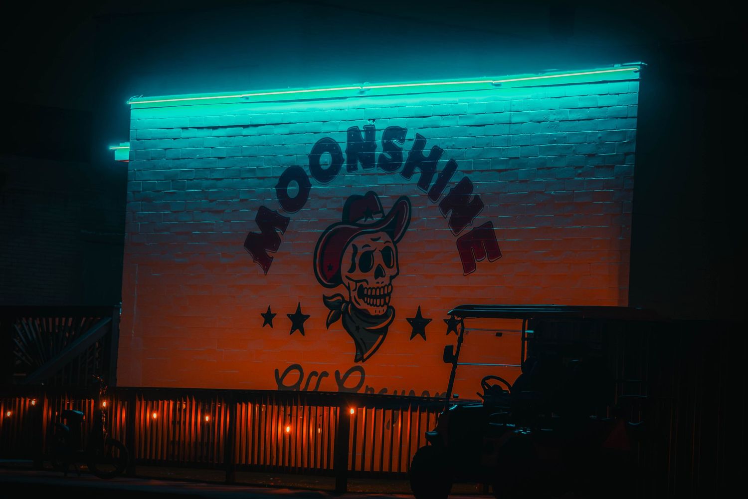 Neon-lit Moonshine bar sign with skull cowboy logo glowing on a brick wall at night.