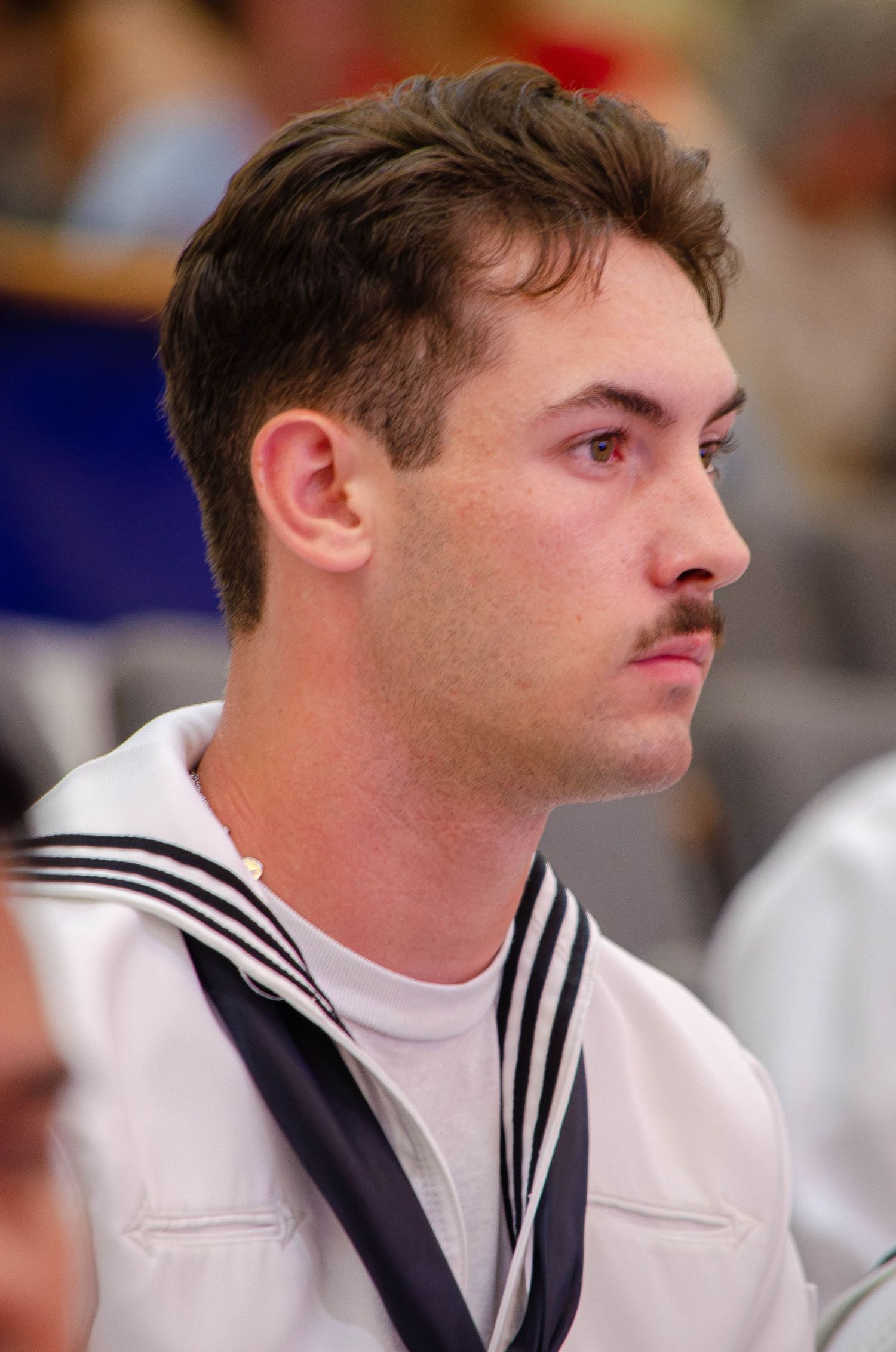 Young male Navy sailor in white uniform with black neckerchief at military event.