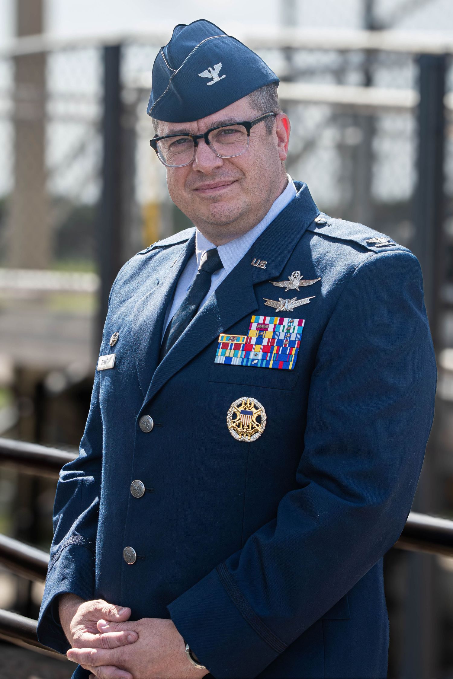 A US Air Force Colonel in dress uniform displays medals and wings at an outdoor ceremony.