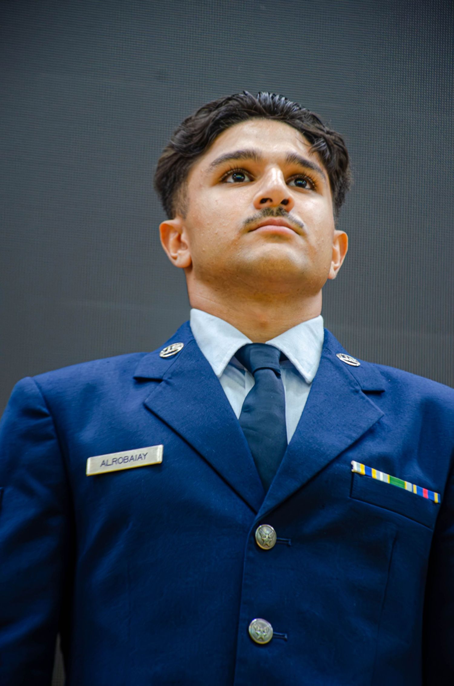 Young male Air Force cadet in blue dress uniform looks upward seriously.