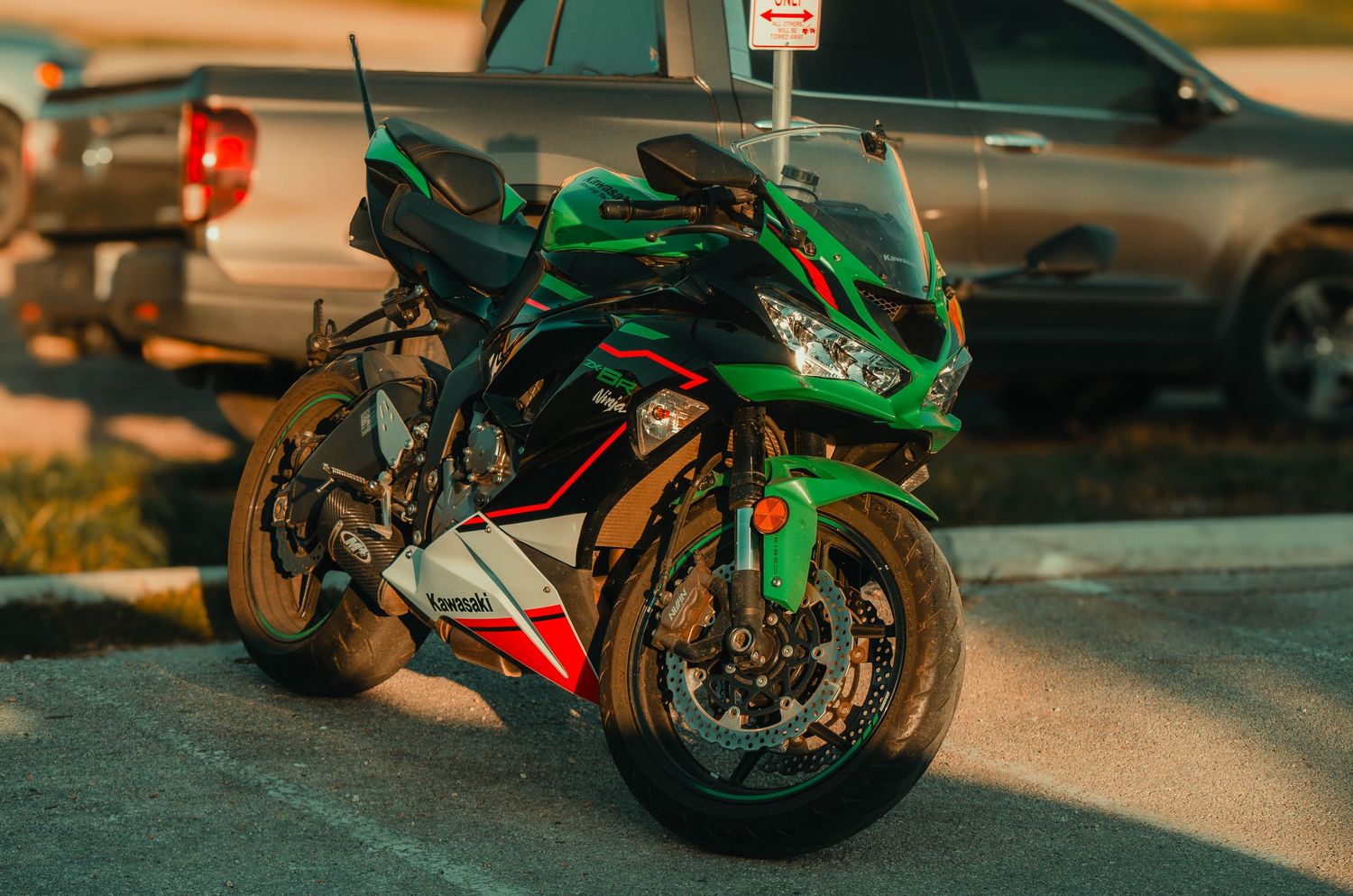 Green Kawasaki sport motorcycle parked in a lot beside a truck, showcasing its sleek fairing and performance design.