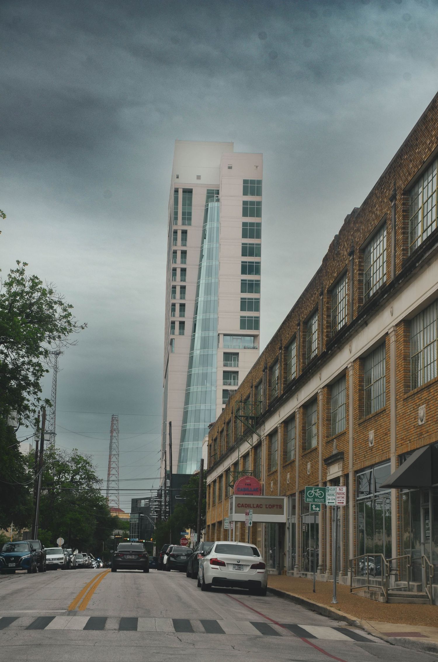 Street view of brick buildings leading to a modern glass skyscraper under dramatic storm clouds.