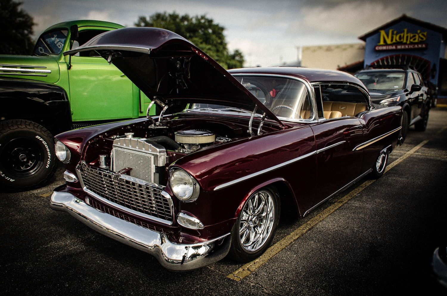 A restored 1955 Chevy Bel Air in deep burgundy with chrome details and open hood at a classic car show.
