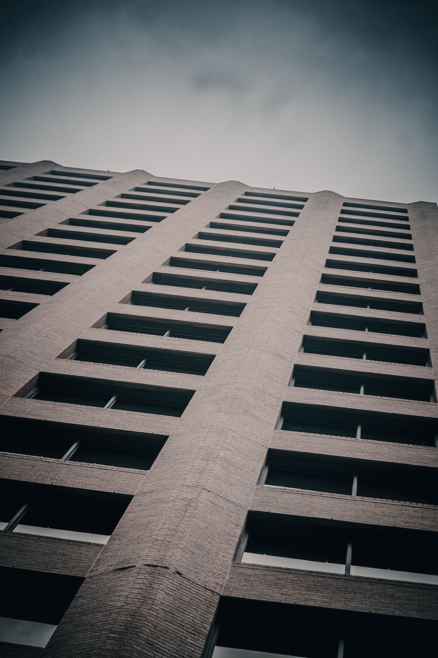 Low angle view looking up at a tall brutalist concrete building facade against cloudy sky.