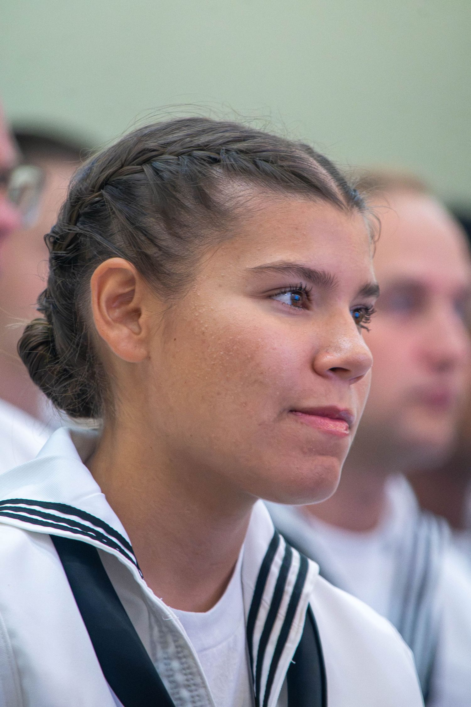 Young female US Navy sailor with braided hair in white uniform looking ahead.