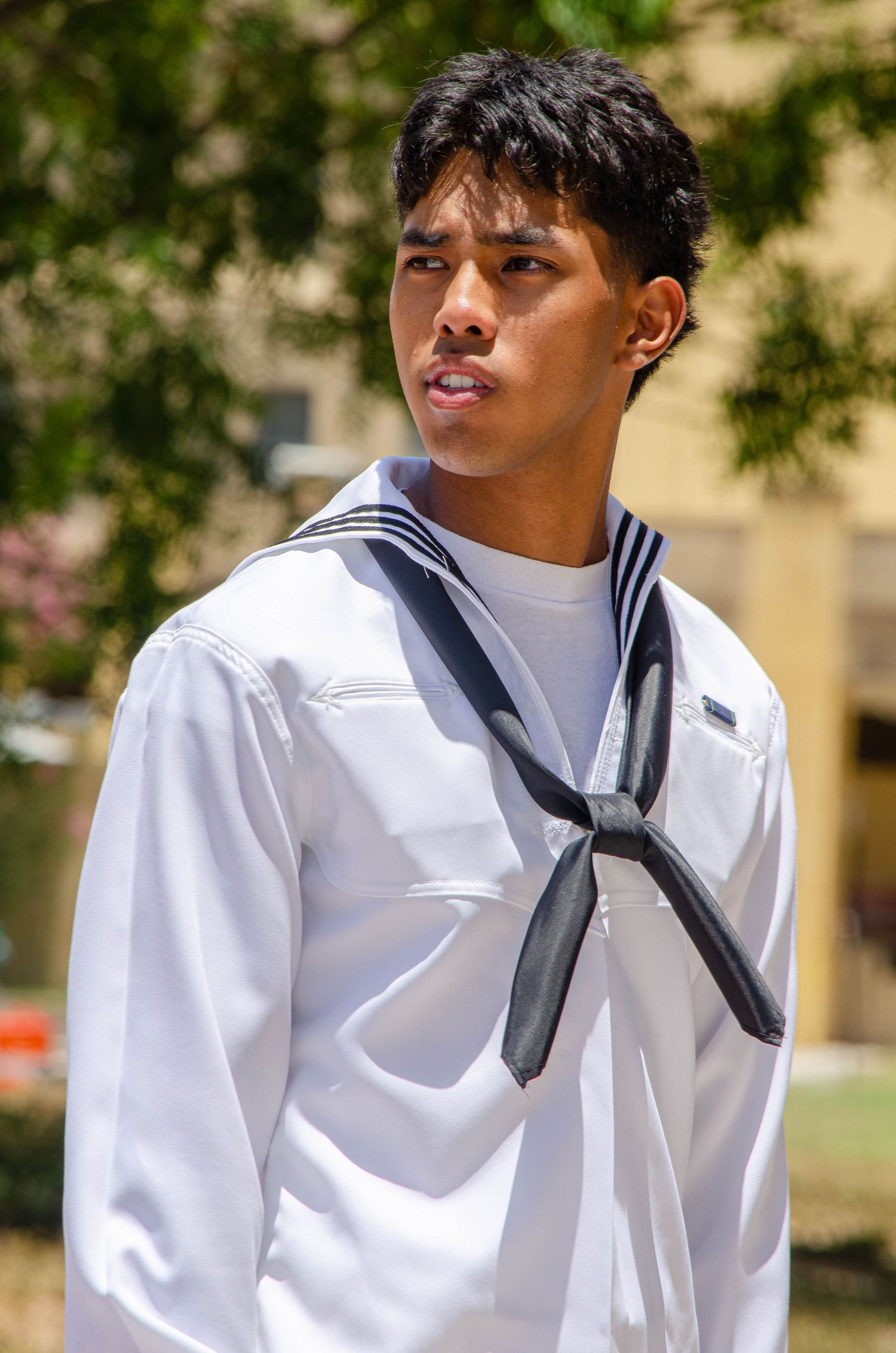 Young male Navy recruit in white sailor uniform standing outdoors in sunlight.