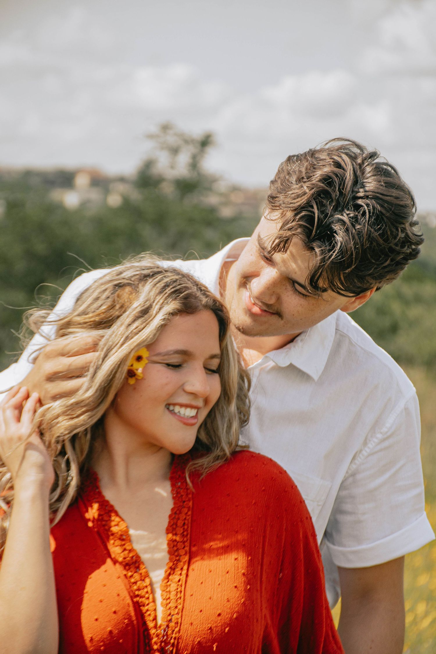 Young man tenderly placing a flower in smiling womans hair in a sunlit green field.