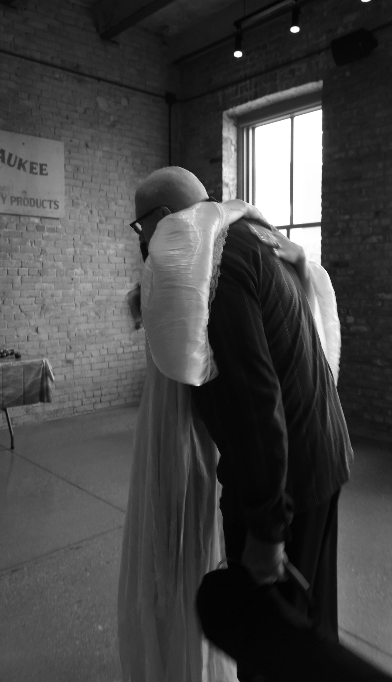 Black and white photo of bride and guest sharing hug at wedding ceremony.
