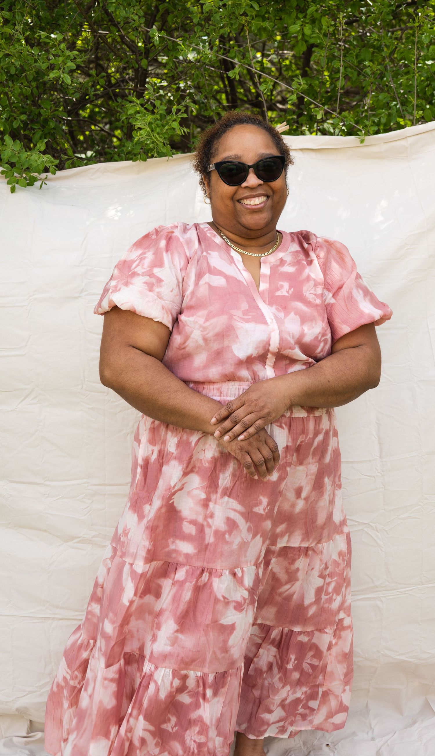 Woman in a pink floral dress posing outdoors wearing sunglasses