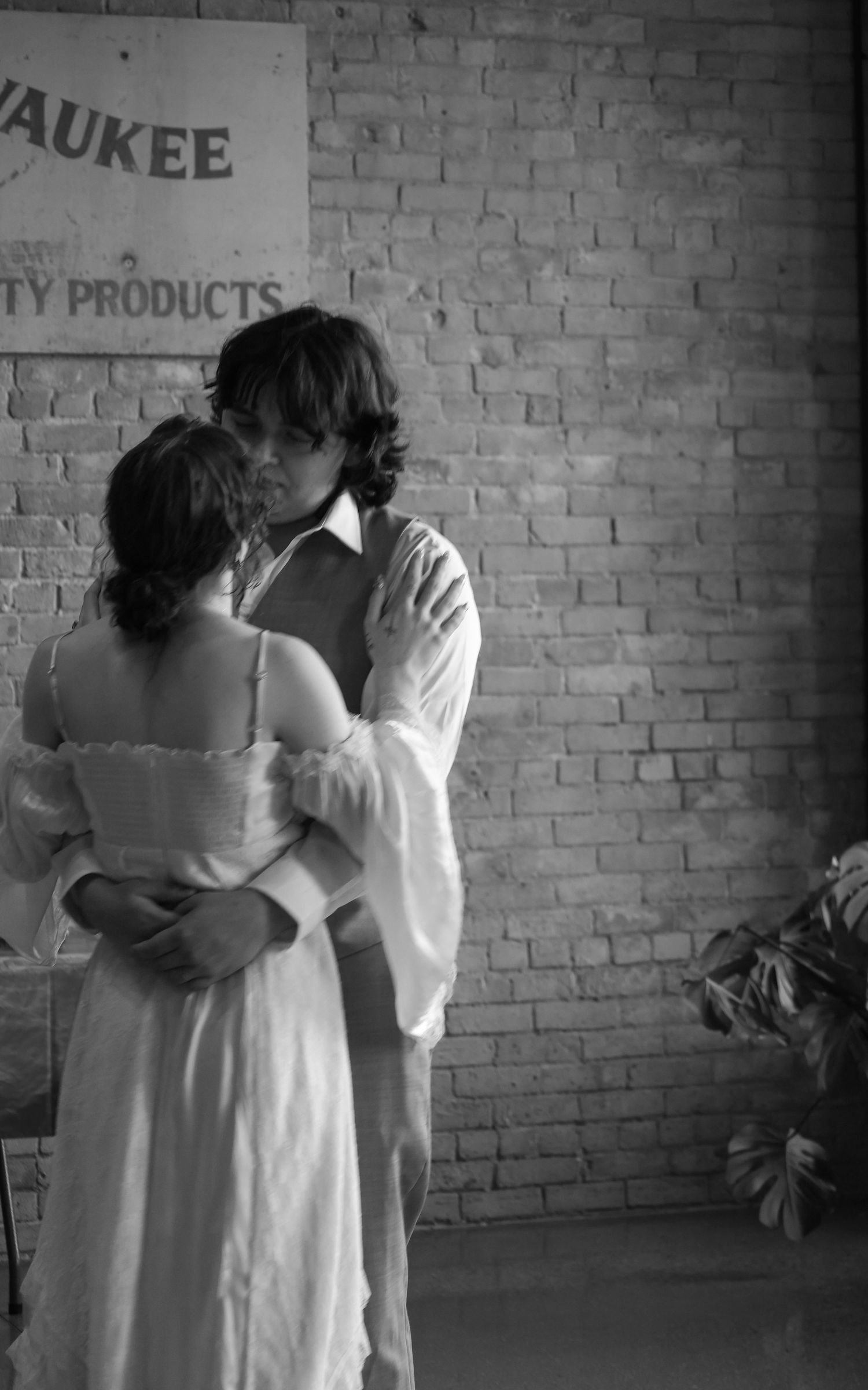 Black and white romantic couple embracing kissing near Milwaukee brick wall vintage sign.