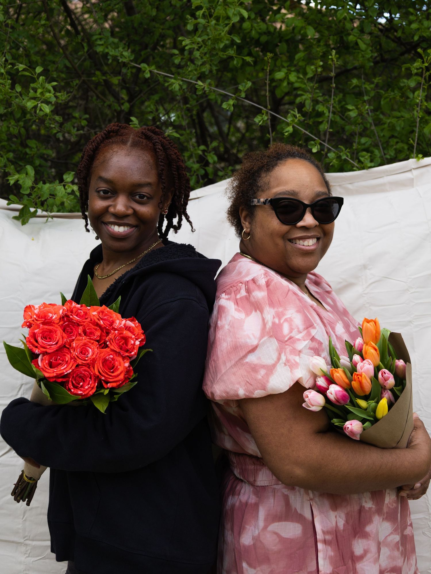 Two women posing outdoors holding flower bouquets