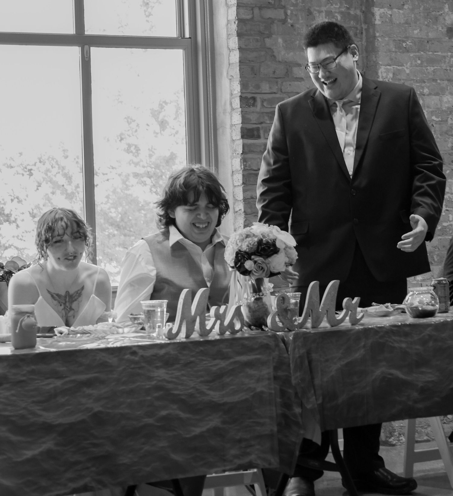 Black and white photo of wedding couple laughing at sweetheart table with Mr Mrs signs.