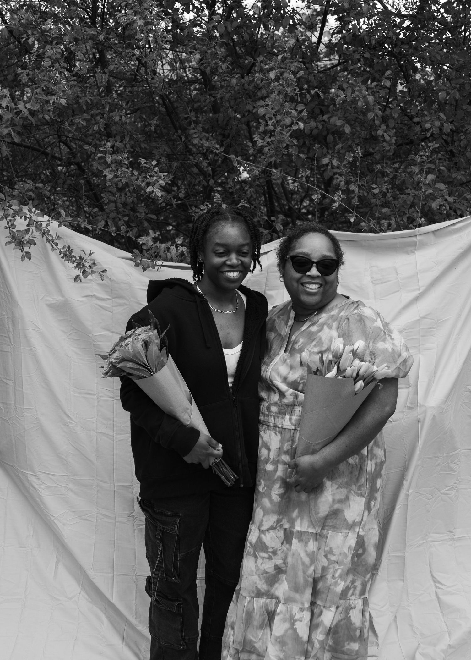 Black and white portrait of two women posing outdoors holding flower bouquets