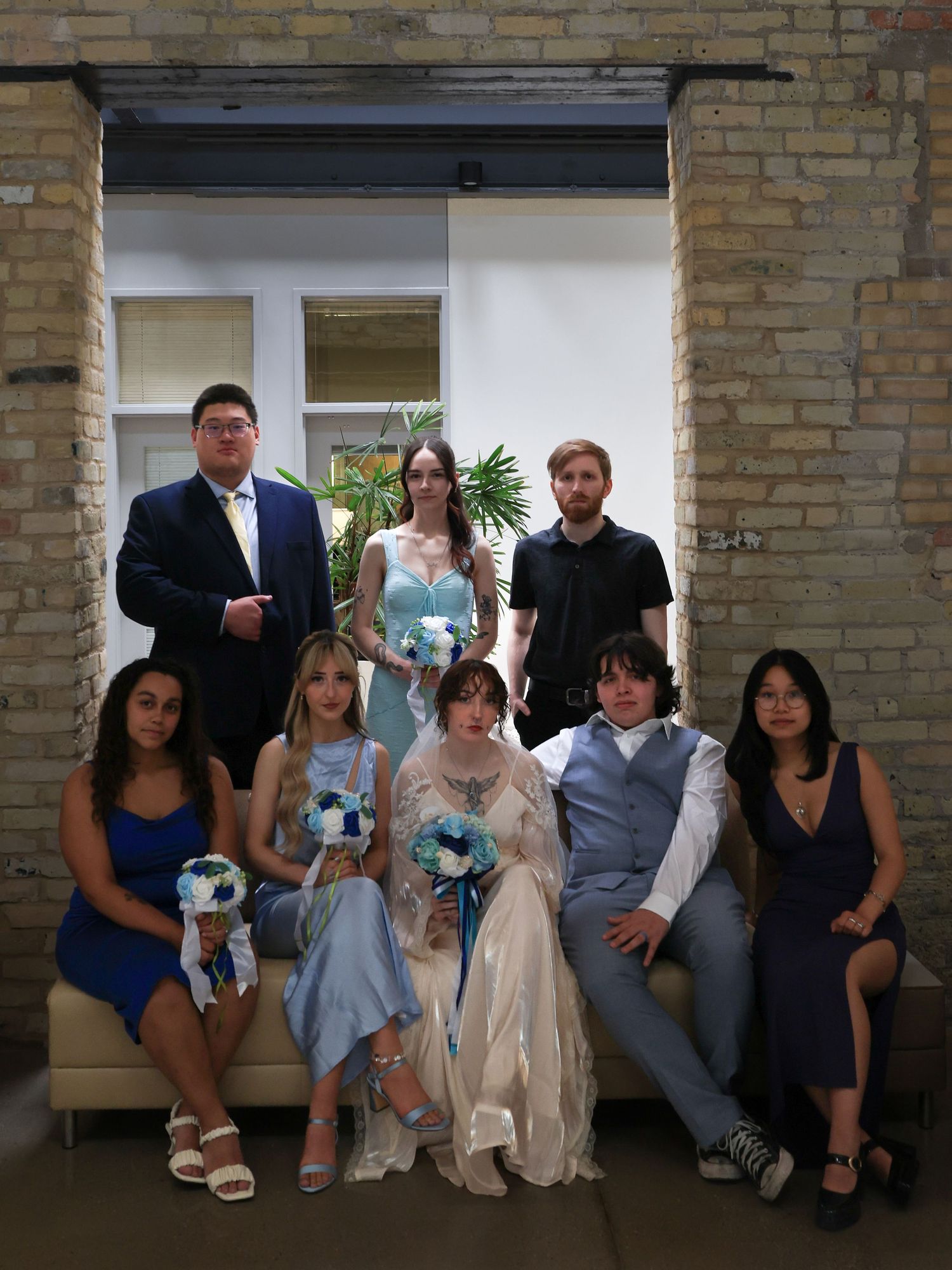 Wedding party group photo with bride groom bridesmaids groomsmen in blue attire brick venue.