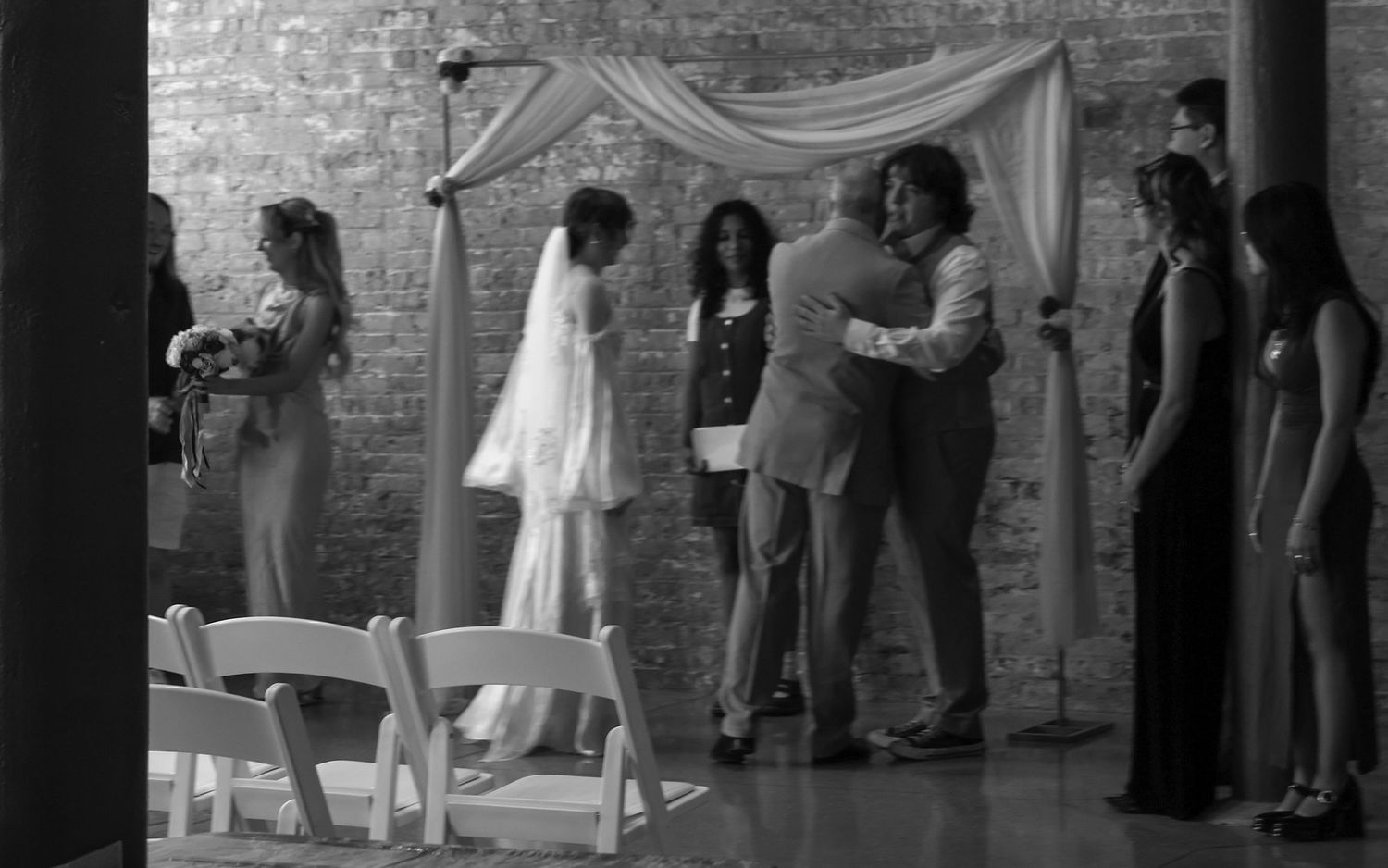 Black and white wedding ceremony with bride and groom hugging under draped arch altar.