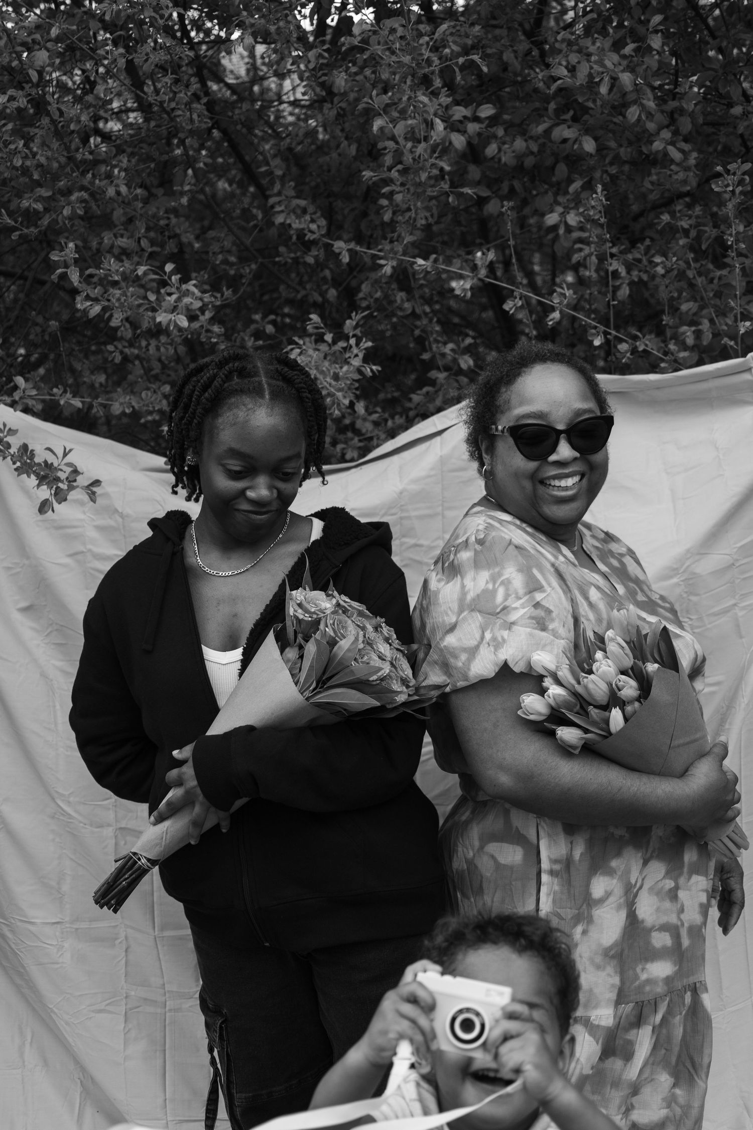Black and white photo of two women and child holding flowers outdoors.
