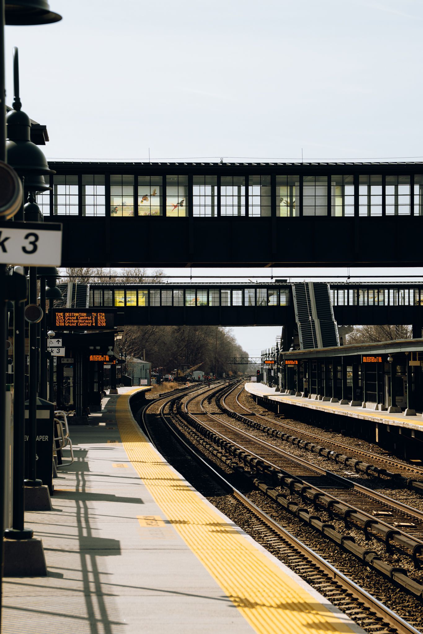 Quiet commuter rail station platform with curved tracks and illuminated departure board.