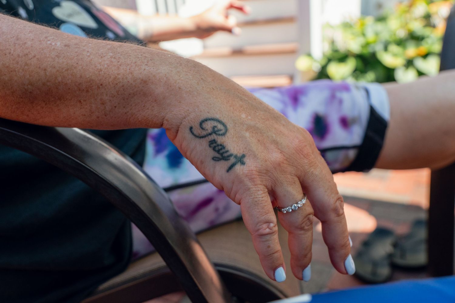 Close-up of a hand with a cursive tattoo reading Grayt wearing a diamond ring.