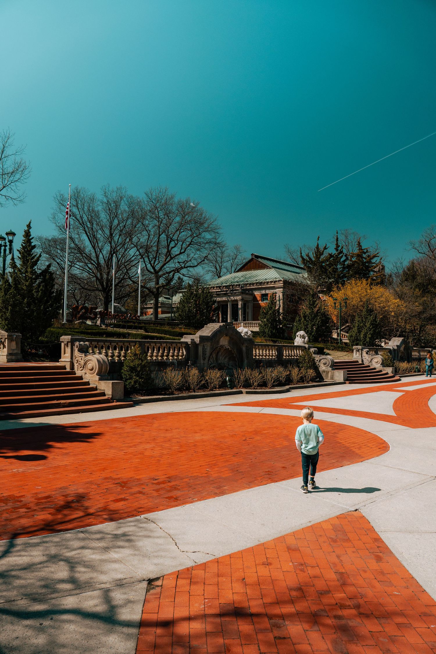 Person walking across ornate red brick plaza toward a historic domed building on a sunny day.