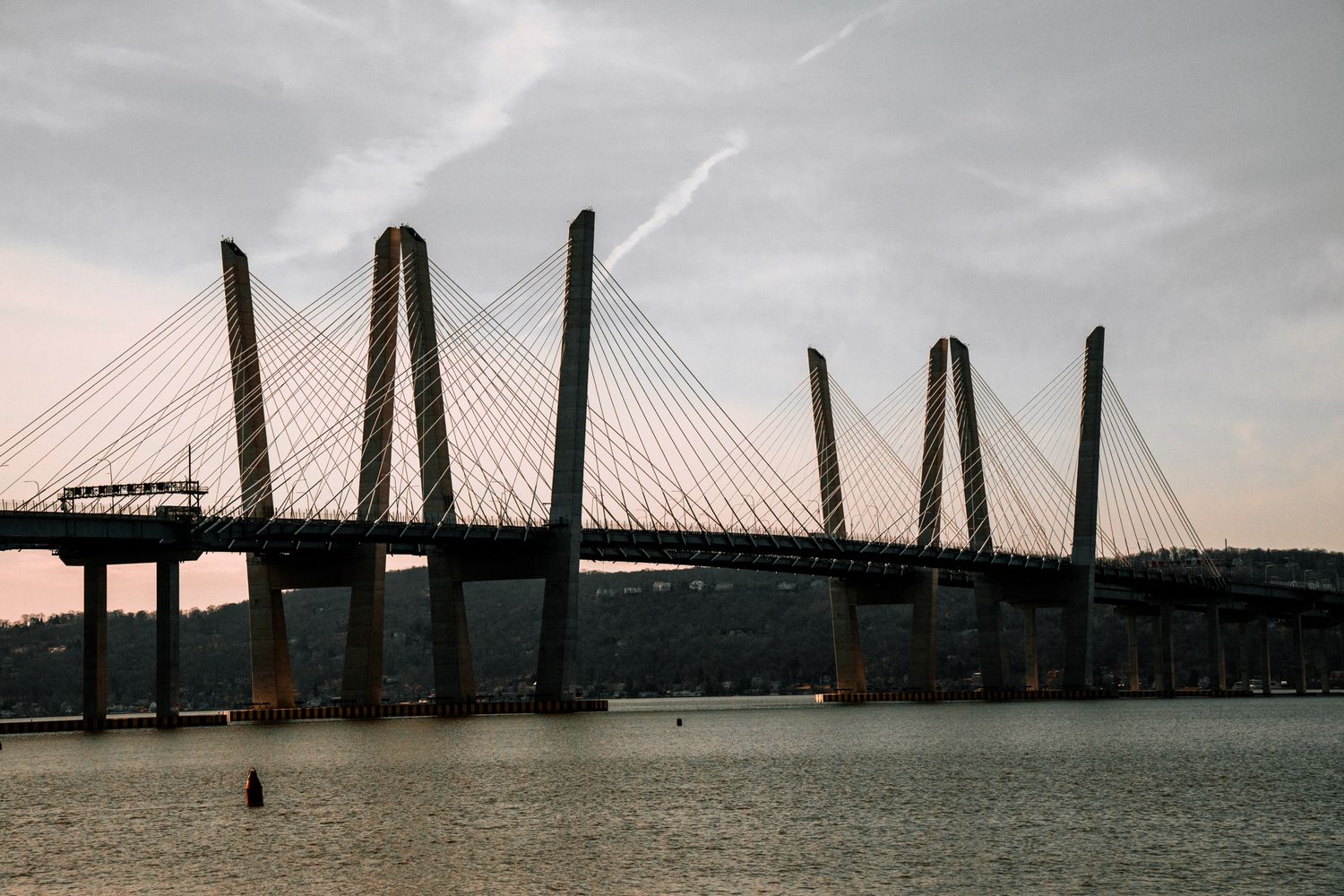 Low-angle view of a large cable-stayed bridge over a river under an overcast evening sky.