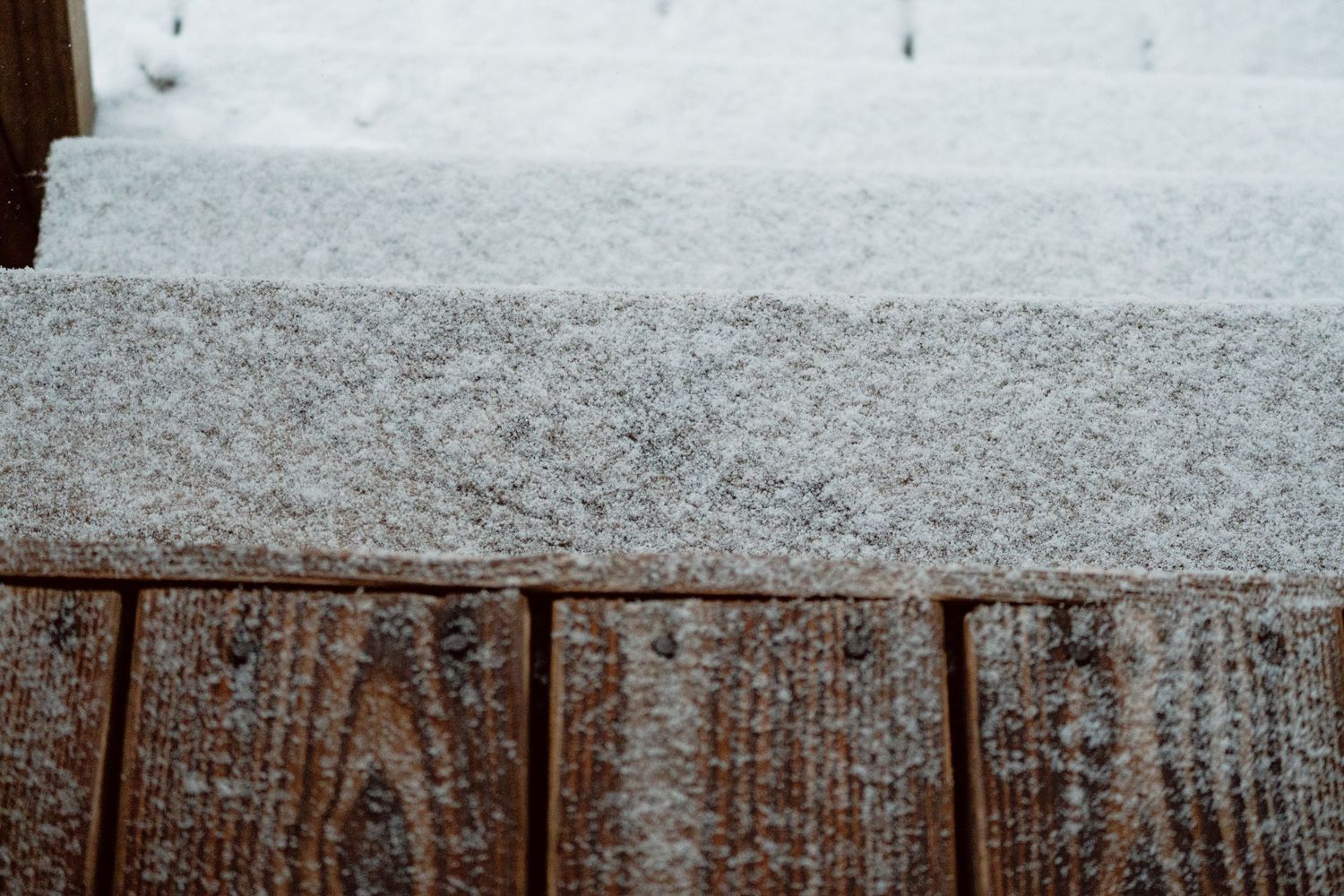 Close-up of fresh white snow accumulating on a rustic wooden deck railing.