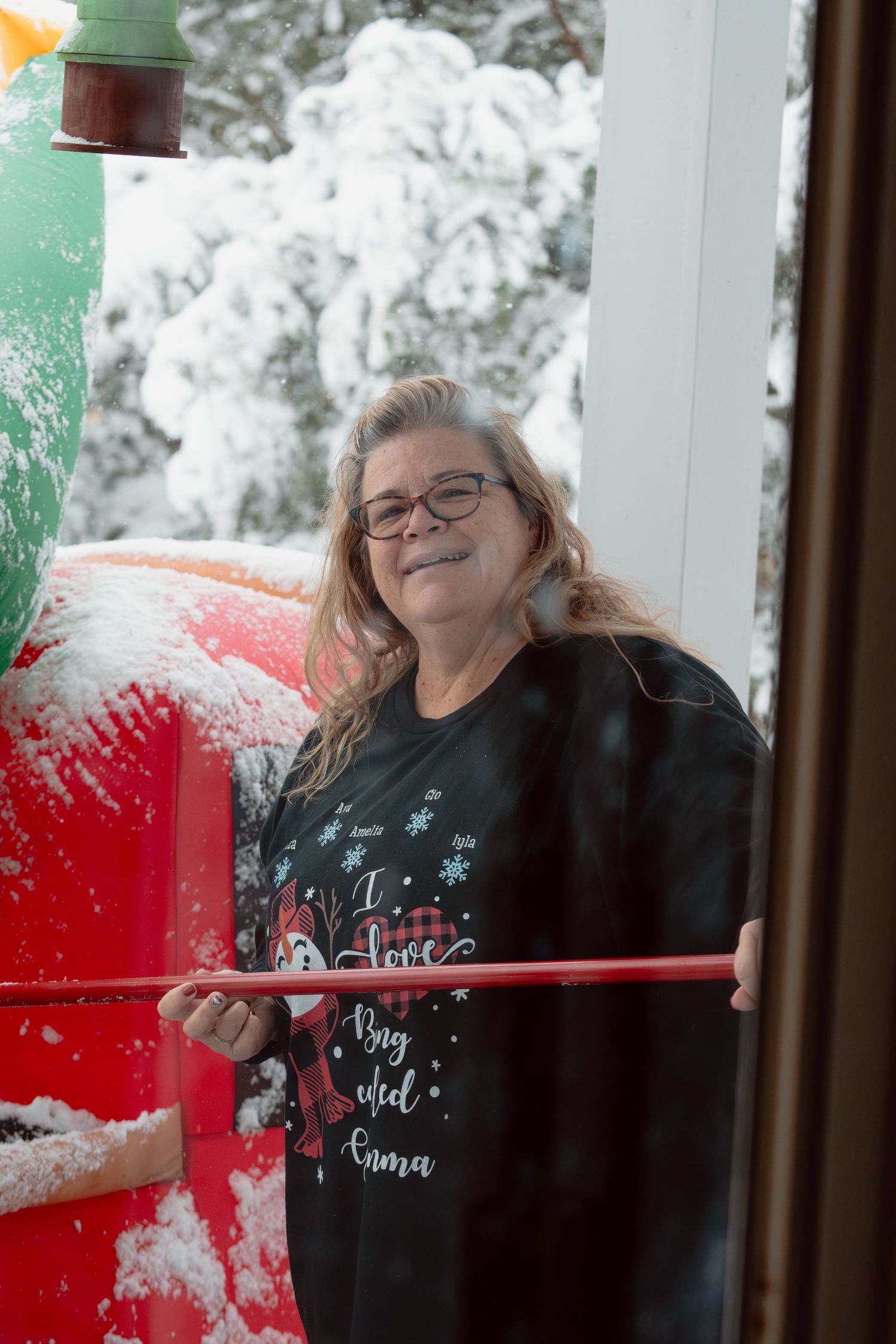 A smiling woman in a Christmas sweater standing beside a snow-covered inflatable holiday decoration.