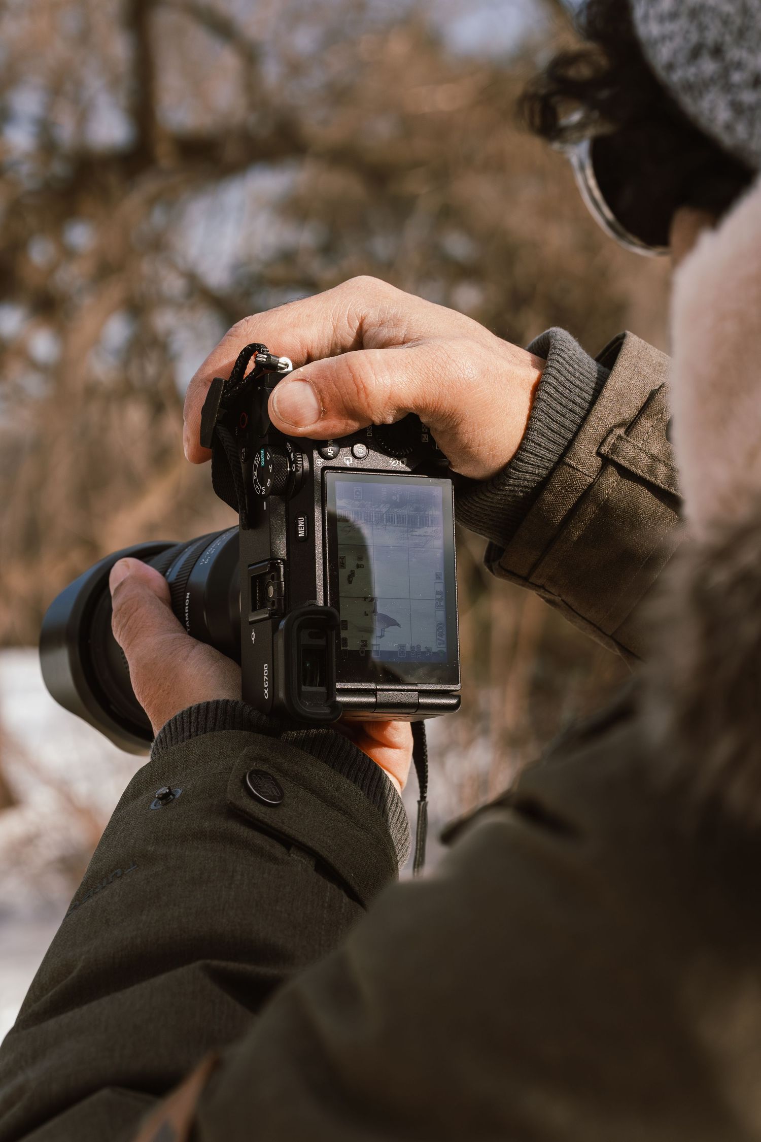 Man in winter jacket using a DSLR camera with articulating screen to photograph outdoors in snowy conditions.