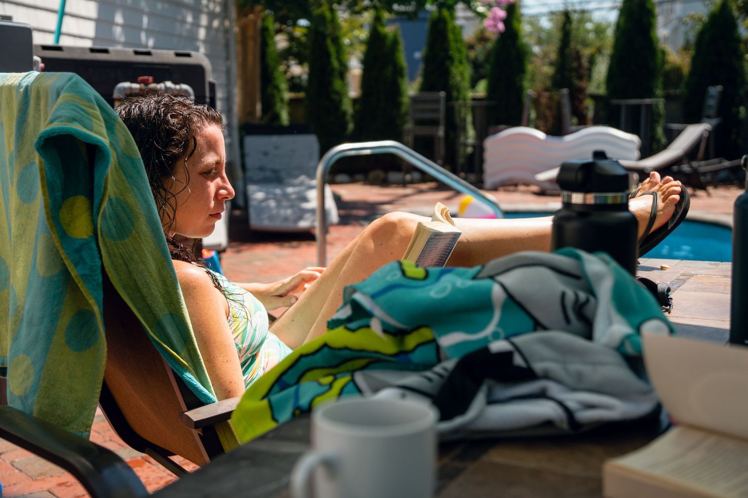 Woman relaxing on a lounge chair by a backyard pool on a sunny day with a colorful towel.