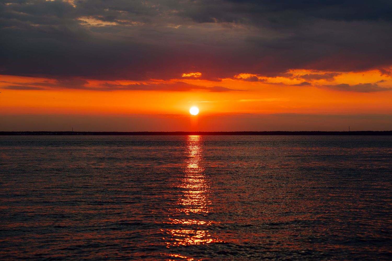 Stunning ocean sunset with vibrant orange and red sky reflecting on calm water.