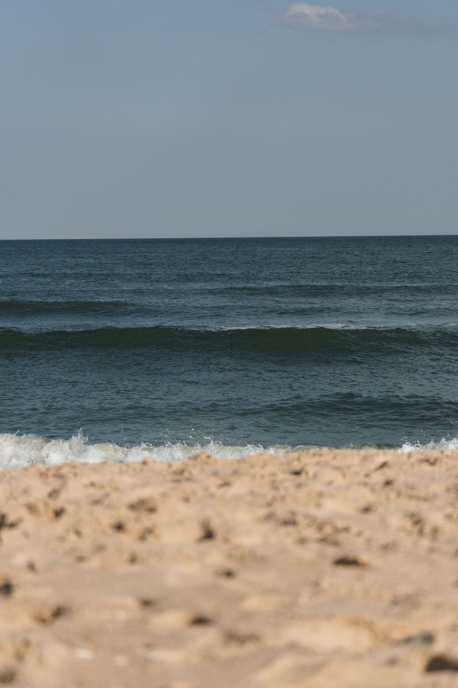 Sandy beach with rolling ocean waves and a partly cloudy sky in the background on a calm day.