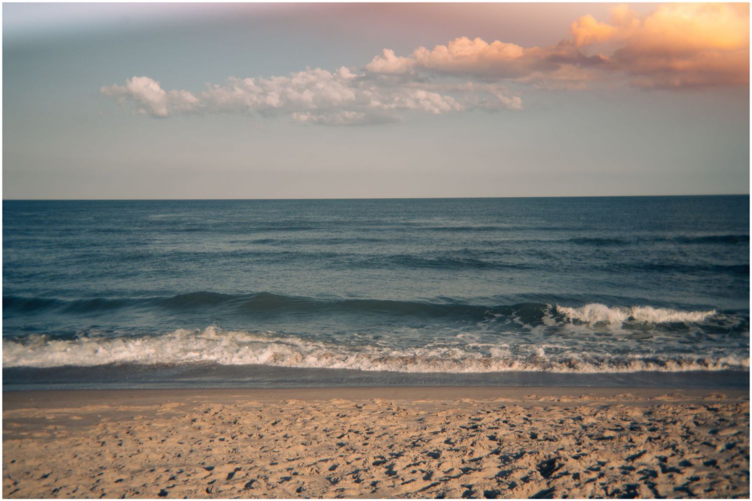 Peaceful ocean waves rolling onto a sandy shore at sunset with colorful clouds above.