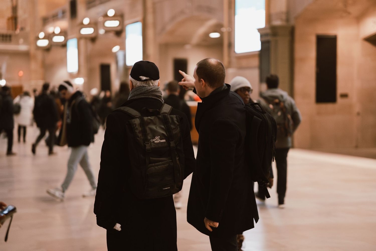 Two people stand in Grand Central Terminal, one pointing directions in the busy hall.