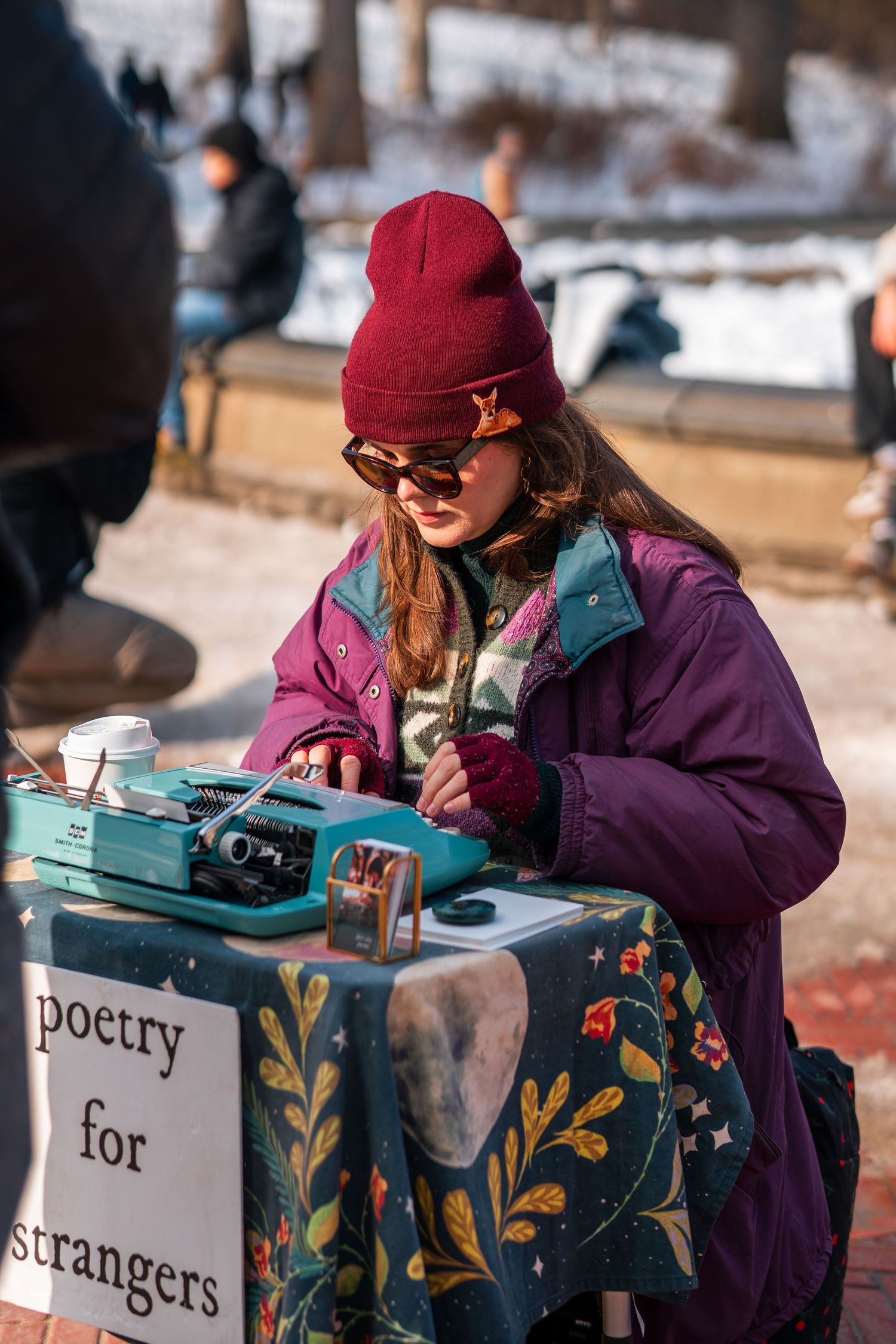 Young woman typing poetry on vintage typewriter at outdoor poetry for strangers table in winter park.
