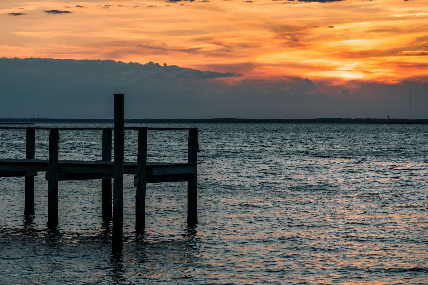 Silhouette of a wooden dock pier against a stunning orange sunset over calm bay waters.