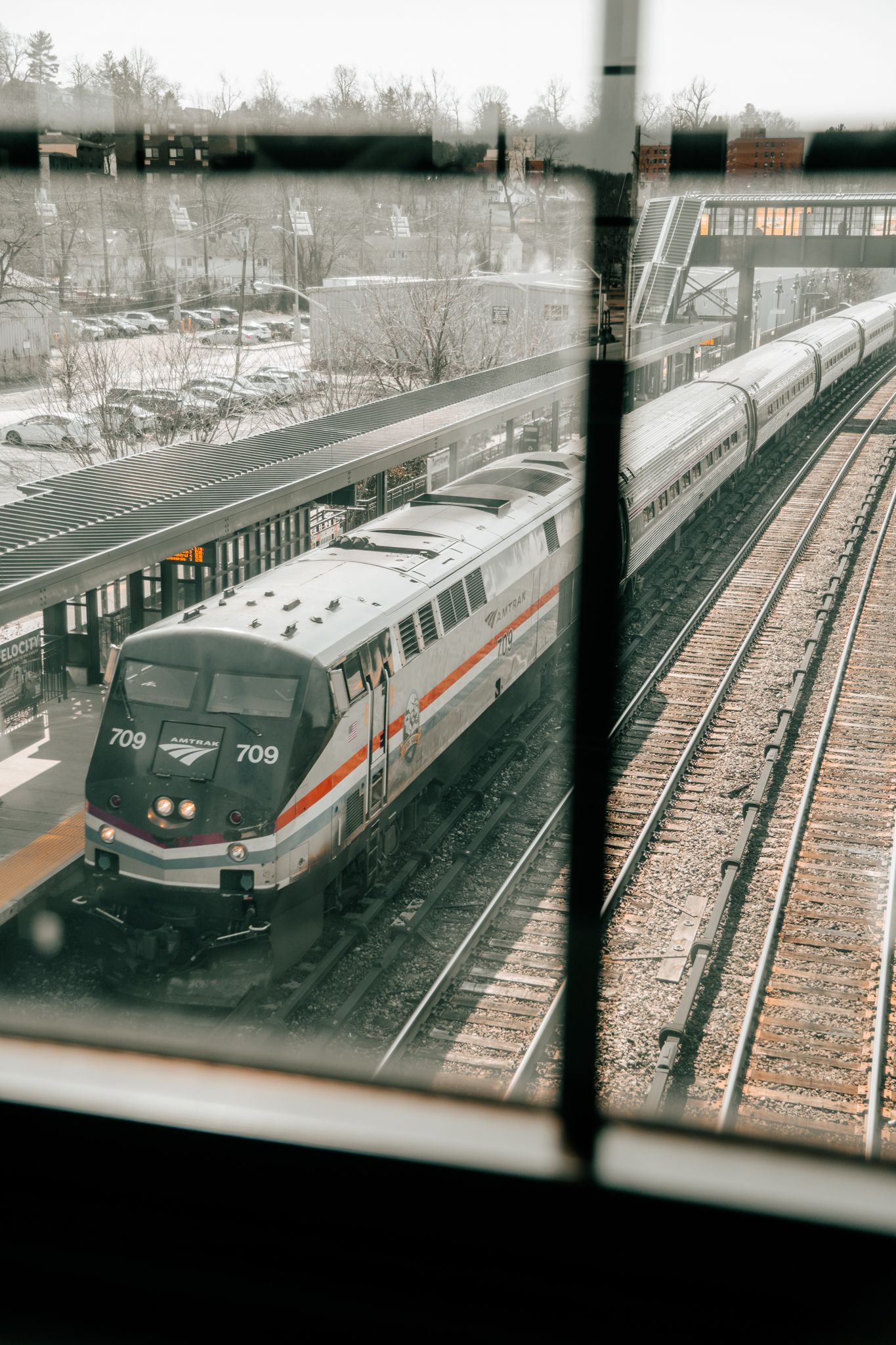 Amtrak train number 709 arriving at a snow-dusted station platform, viewed through a window on a winter day.