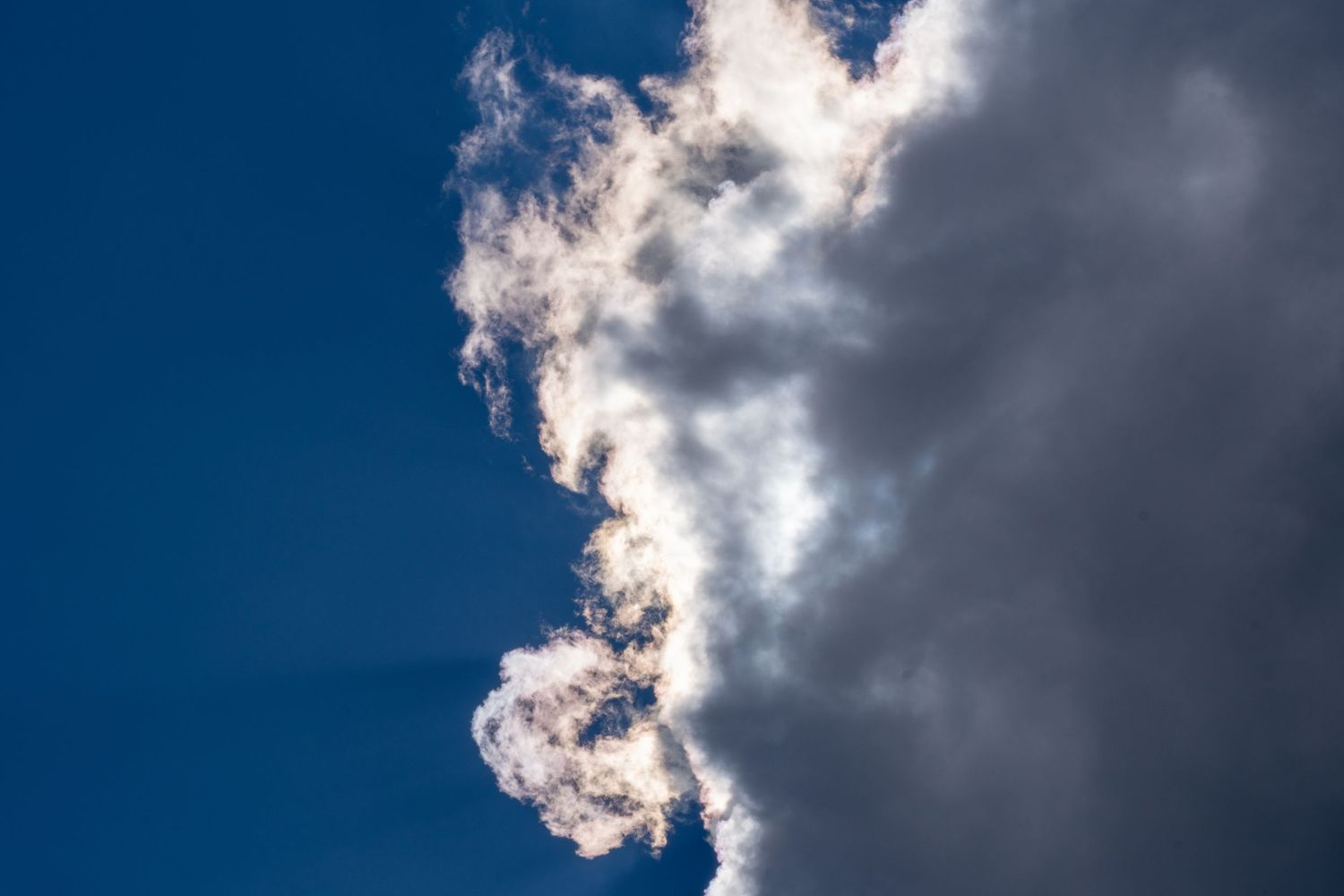 Dramatic white cloud illuminated by sunlight against a deep blue sky.