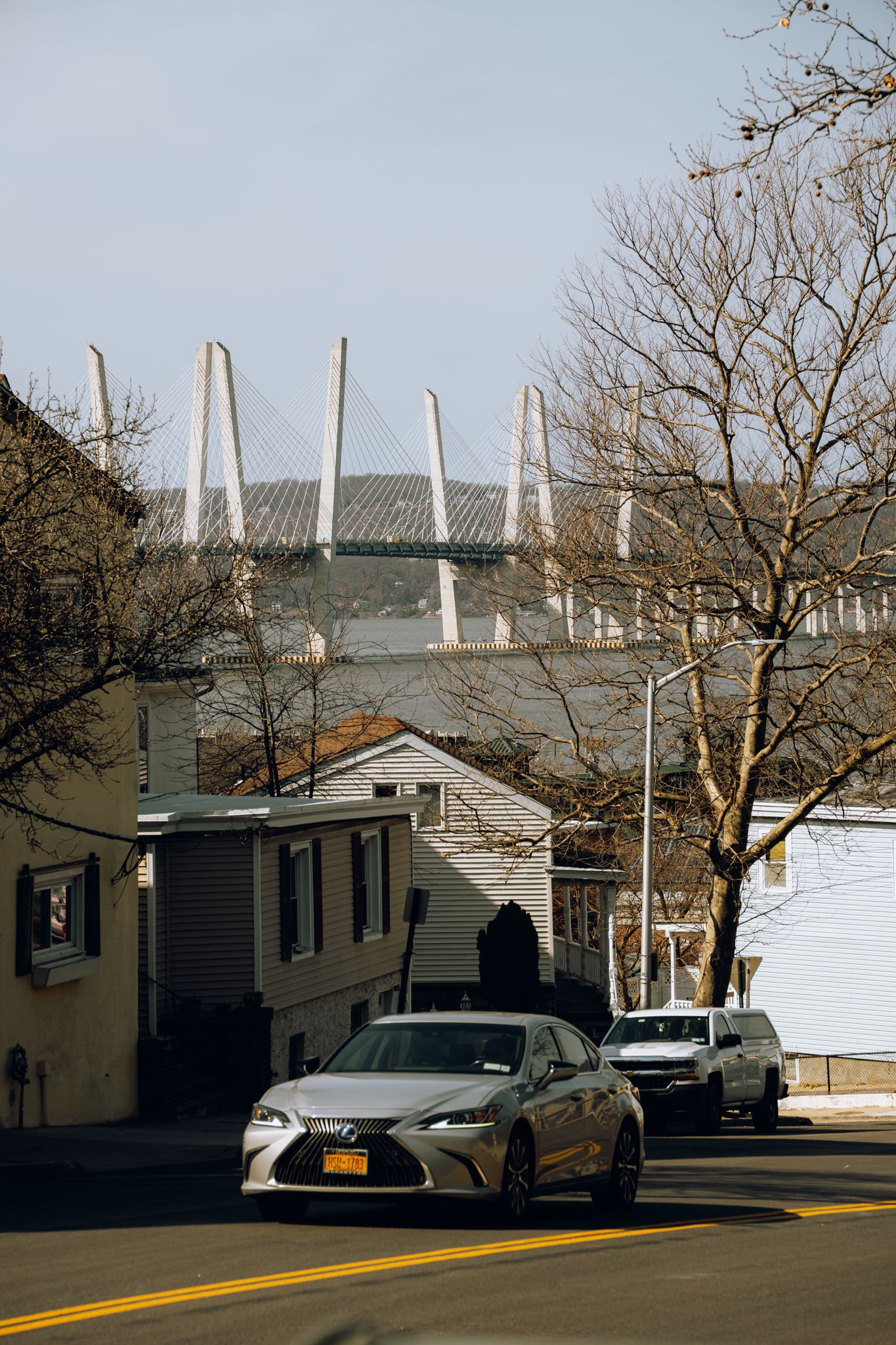 A silver Lexus sedan parked on a street with the Mario Cuomo cable-stayed bridge visible in the background.
