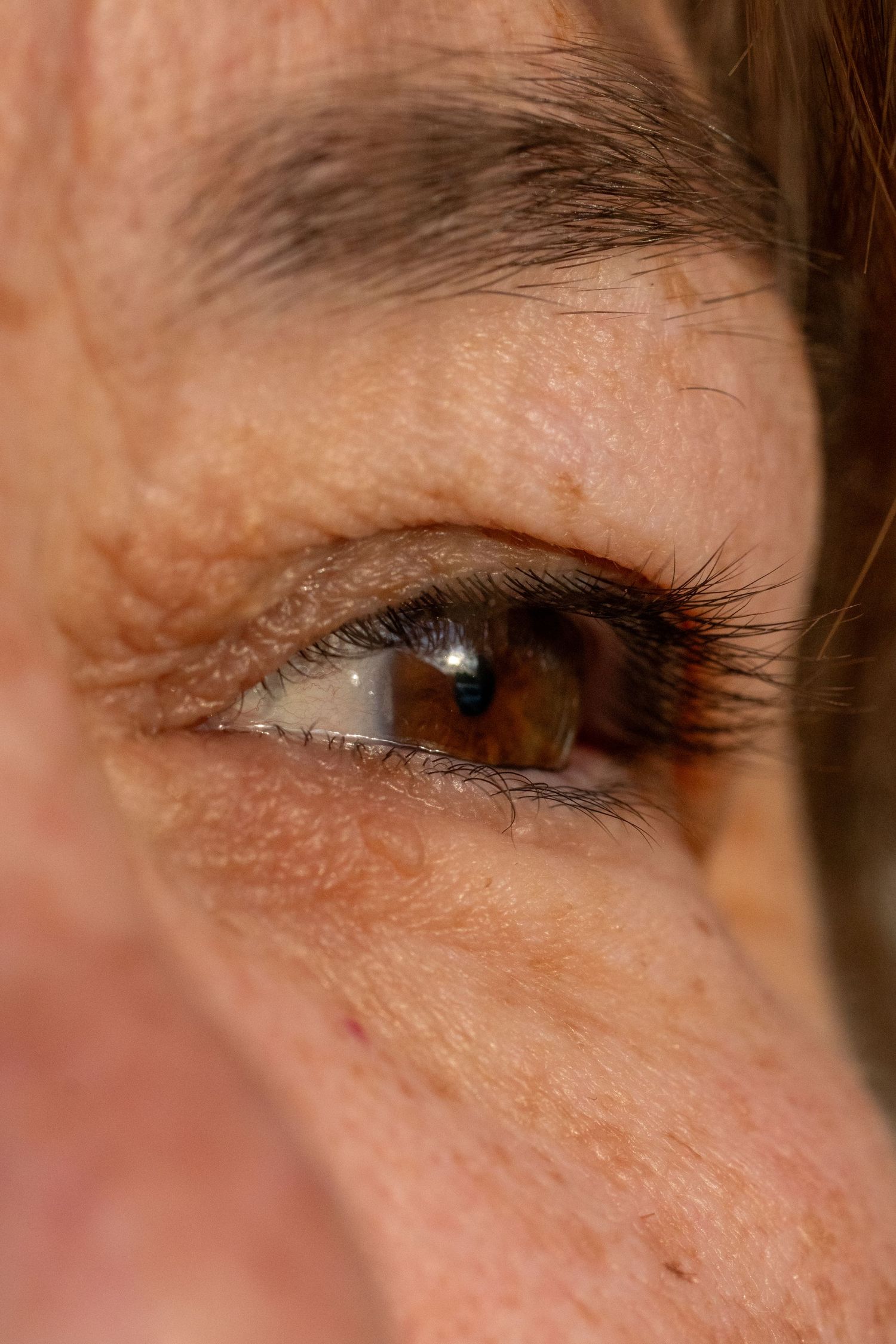Extreme close-up of a brown human eye with visible wrinkles and dark lashes on aged skin.