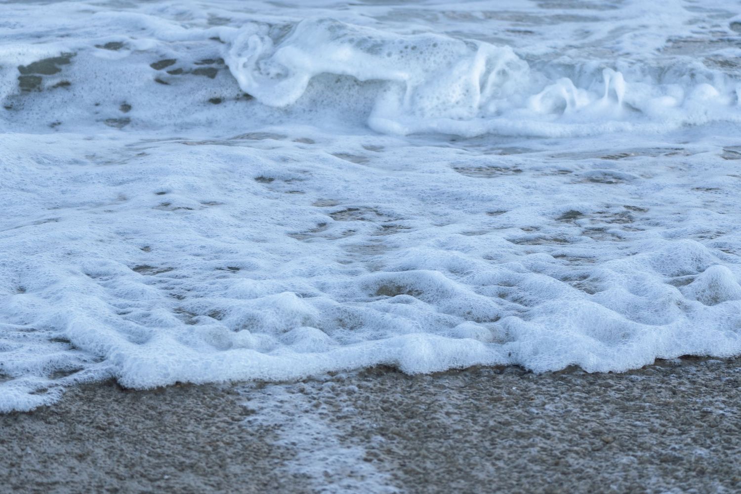 Gentle white sea foam waves washing onto a sandy beach shore.