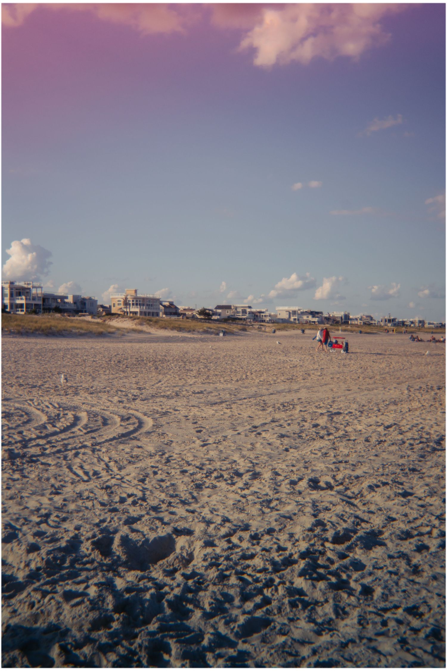 Expansive sandy beach at dusk with beachfront houses and a group of people in the distance.