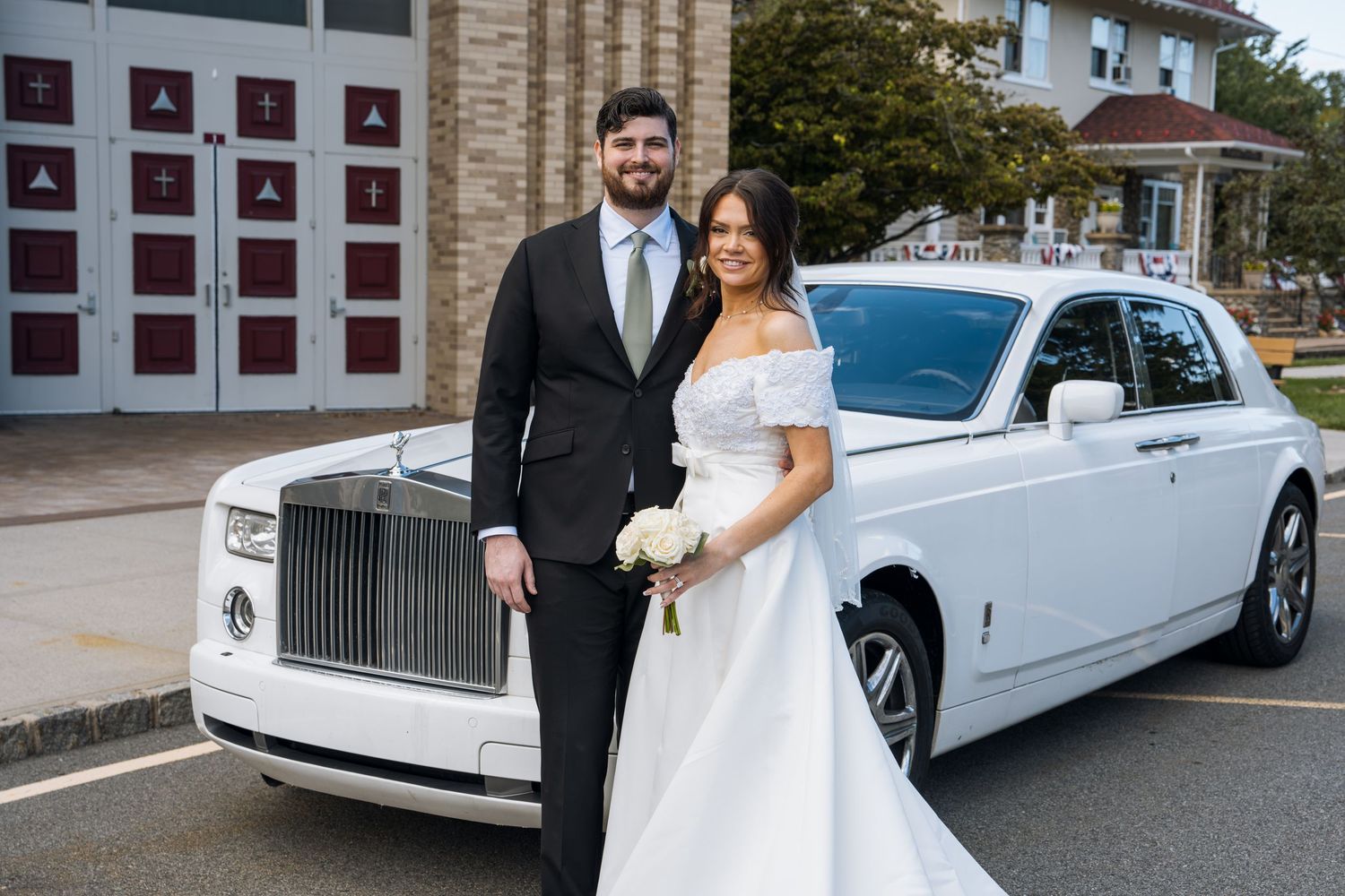 Bride and groom posing in front of a white Rolls-Royce Phantom on their wedding day.