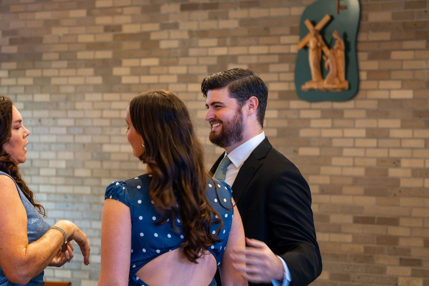 Couple smiling and dancing together at a church reception with brick walls and religious artwork in the background.