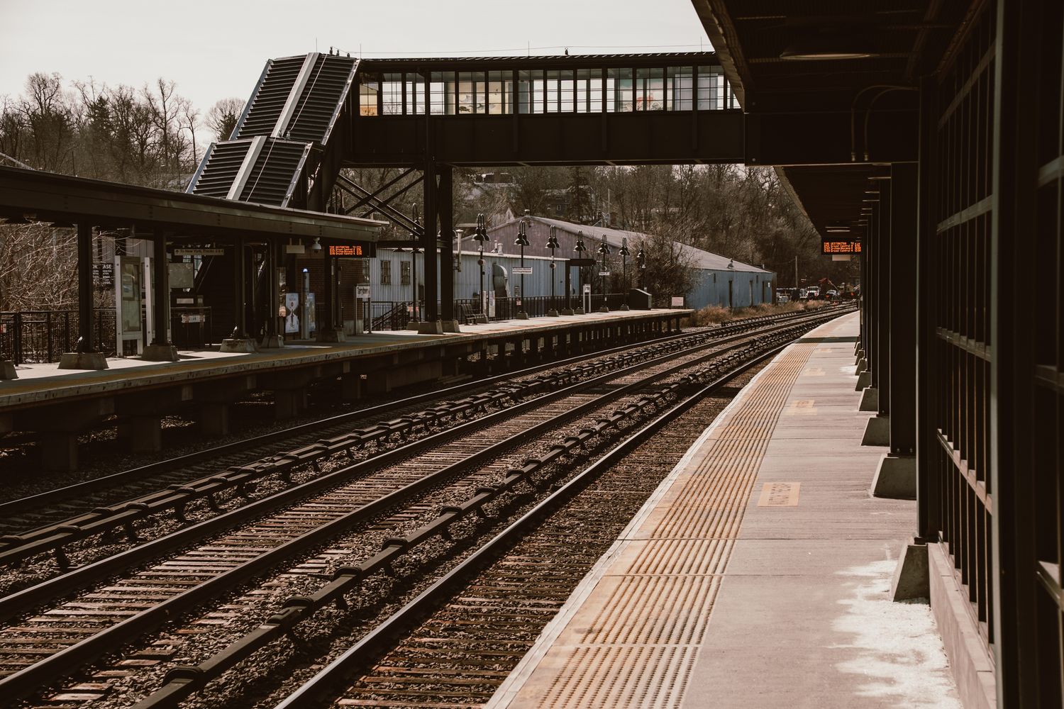 Empty train station platform with multiple railway tracks converging in perspective under a steel bridge structure.