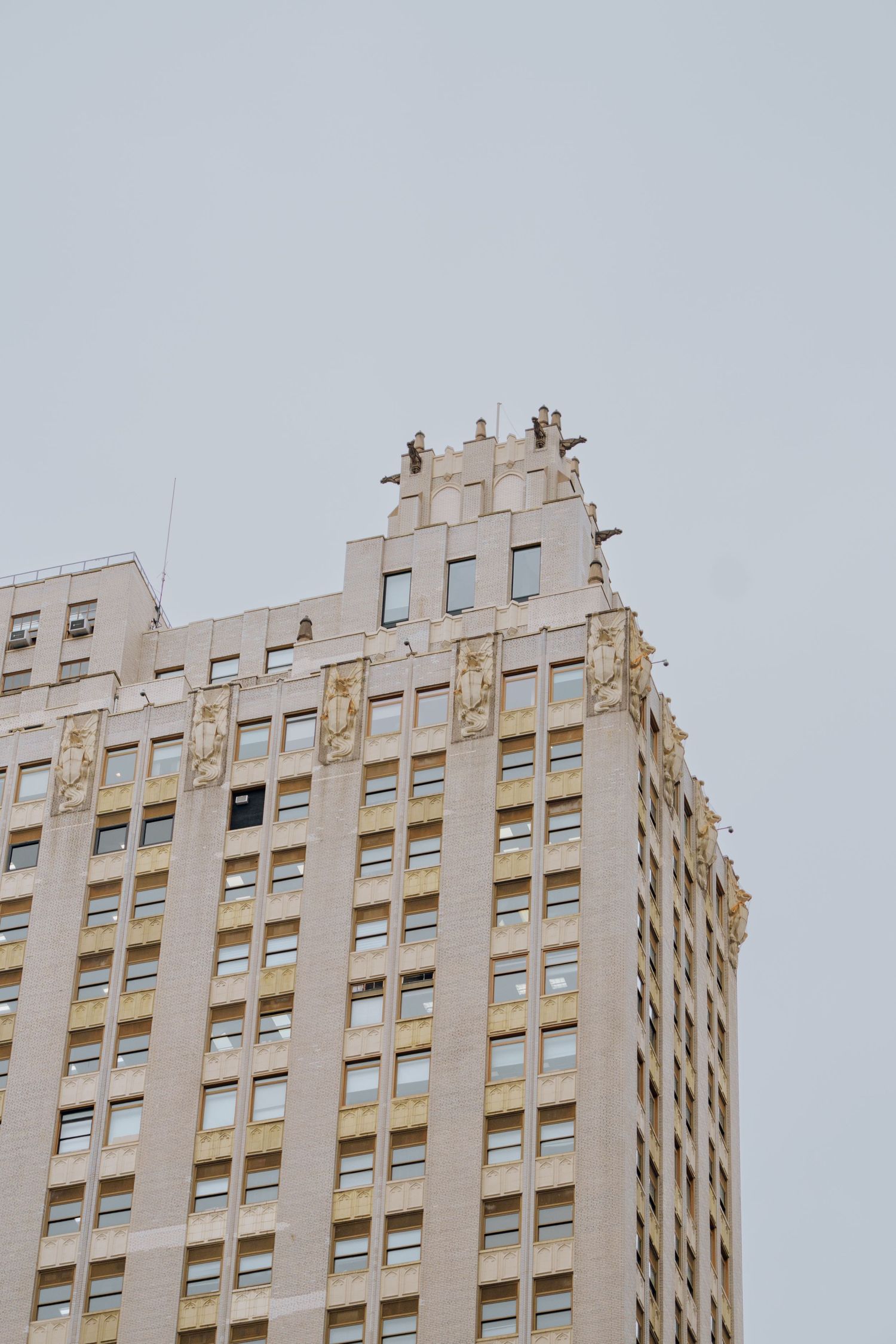 Top of a classic Art Deco skyscraper with decorative crown details against a gray overcast sky in New York City.