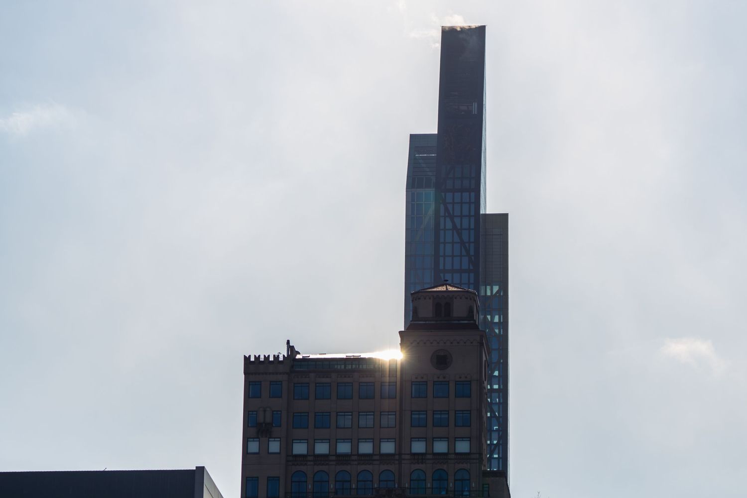Skyscrapers rise above historic brick buildings in a hazy urban skyline with a silhouetted figure on a rooftop.