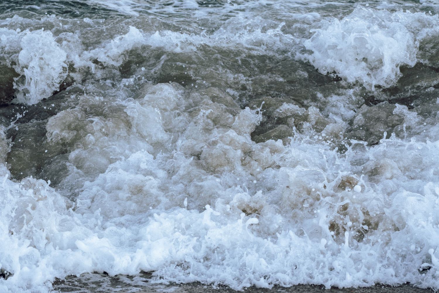Turbulent foamy ocean waves crashing and churning near a sandy beach.