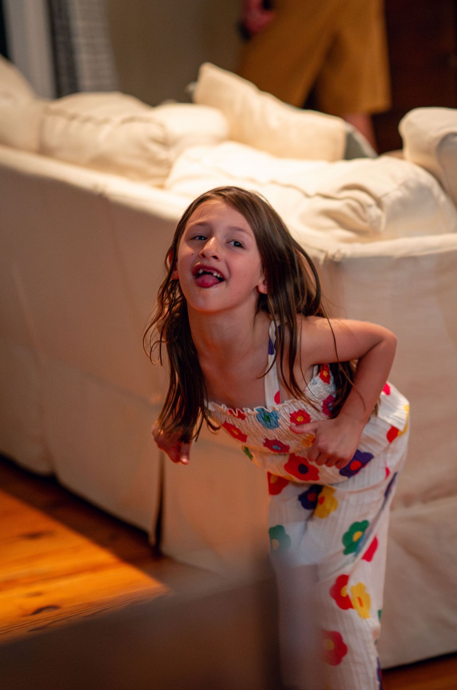 A young girl in a colorful floral dress laughing and dancing in a living room.